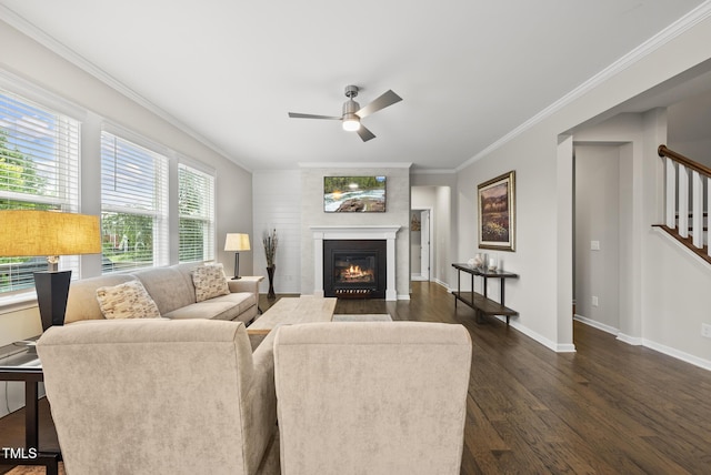 living area with dark wood-type flooring, ornamental molding, a ceiling fan, baseboards, and a glass covered fireplace