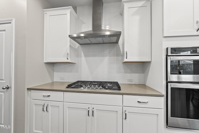 kitchen with wall chimney range hood, stainless steel appliances, decorative backsplash, and white cabinets