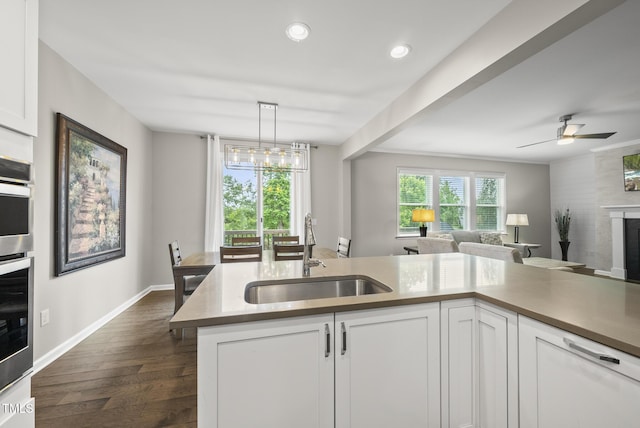 kitchen with a sink, open floor plan, white cabinets, dark wood finished floors, and a fireplace