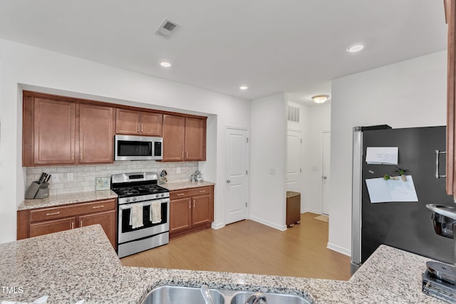 416 Durants Neck Ln, Morrisville, NC 27560 - kitchen with appliances with stainless steel finishes, light wood-style flooring, backsplash, brown cabinets, and light stone countertops