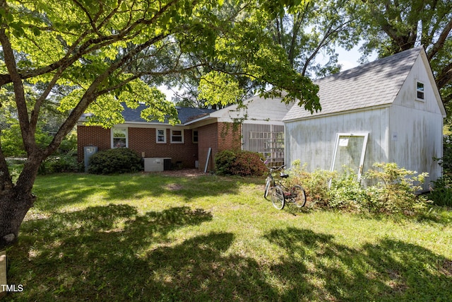 rear view of house with a yard, roof with shingles, and brick siding
