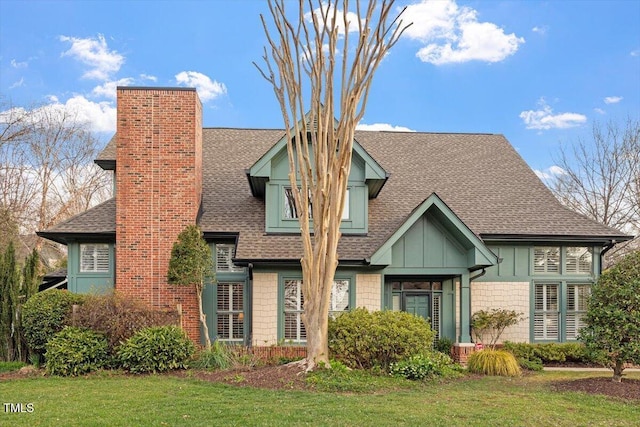 tudor house with a shingled roof, a chimney, and a front yard