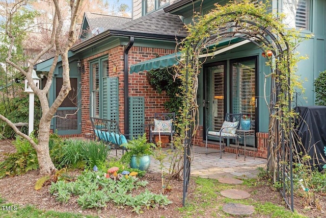 doorway to property featuring brick siding and a shingled roof