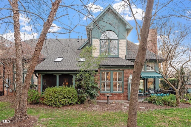 view of front of house with a shingled roof, brick siding, a chimney, and a front lawn