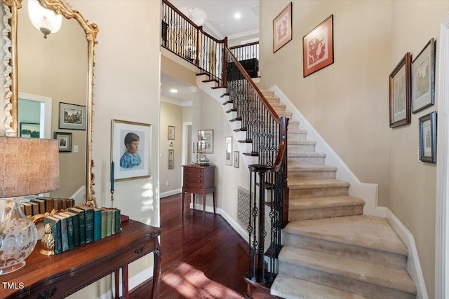 stairs featuring wood finished floors, baseboards, a high ceiling, ornamental molding, and recessed lighting