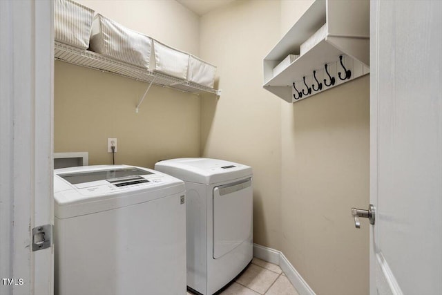washroom featuring washing machine and dryer, light tile patterned flooring, and baseboards