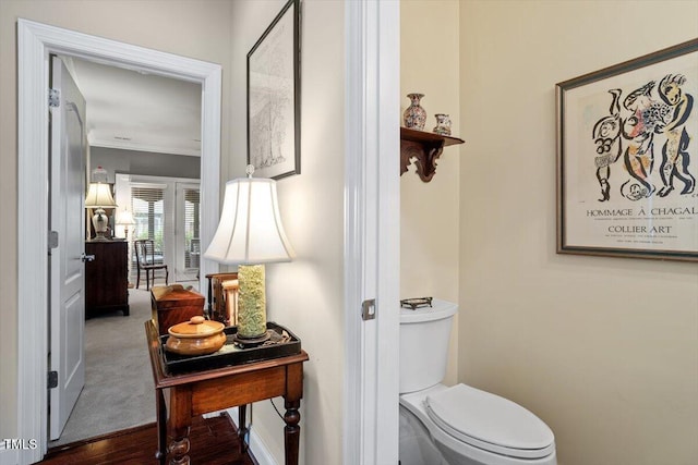 bathroom featuring crown molding, toilet, baseboards, and wood finished floors