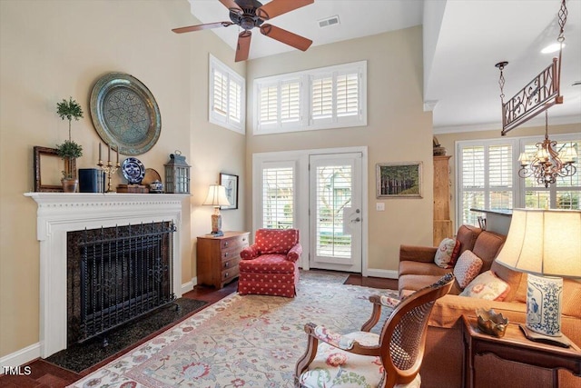 living area with baseboards, a premium fireplace, wood finished floors, a chandelier, and a towering ceiling