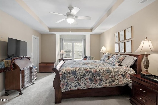 bedroom with light colored carpet, a tray ceiling, and a ceiling fan