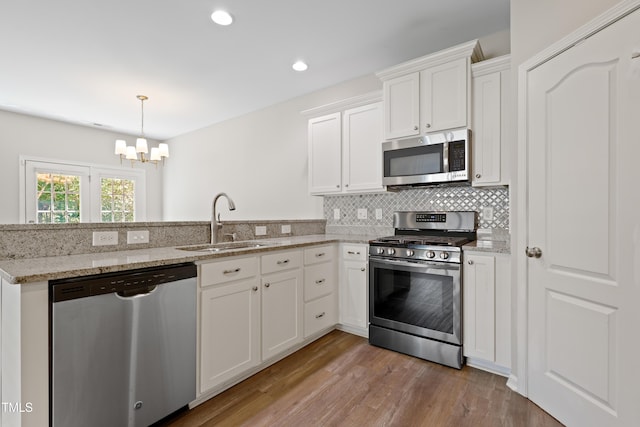 kitchen featuring appliances with stainless steel finishes, a sink, a peninsula, a chandelier, and wood finished floors