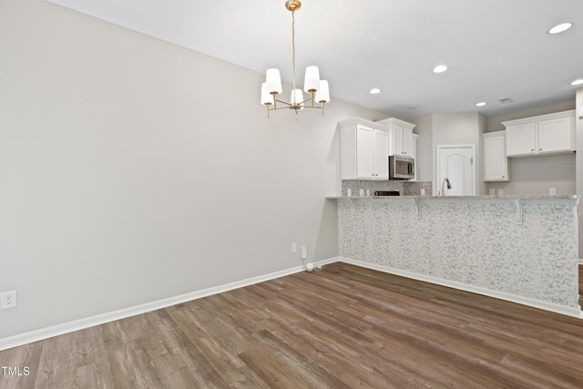 kitchen featuring stainless steel microwave, dark wood-style floors, a peninsula, baseboards, and a chandelier