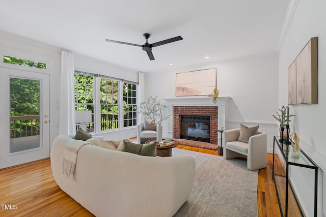 living area featuring light wood-style flooring, a brick fireplace, ornamental molding, ceiling fan, and recessed lighting