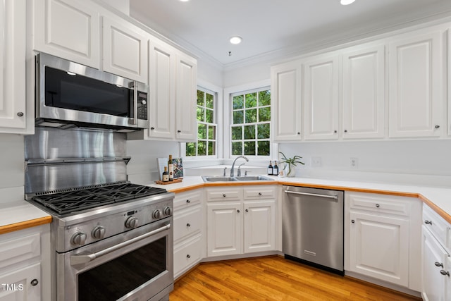 kitchen with stainless steel appliances, a sink, white cabinetry, recessed lighting, and ornamental molding