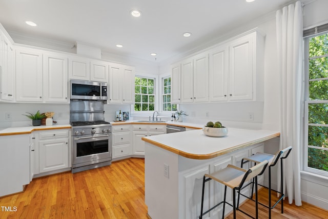 kitchen with appliances with stainless steel finishes, a sink, a peninsula, white cabinets, and recessed lighting