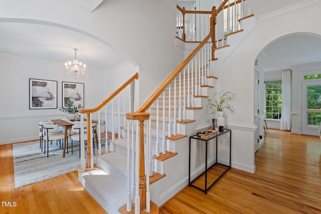 staircase with arched walkways, wood finished floors, a chandelier, and crown molding