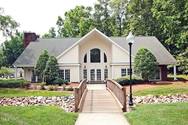 view of front facade with french doors, a chimney, a front lawn, stucco siding, and a shingled roof