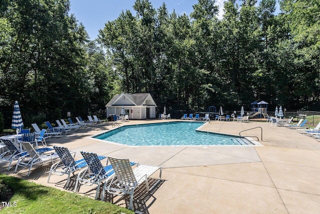 community pool with fence, a patio area, and view of wooded area