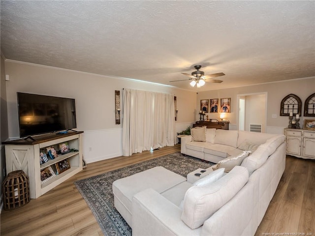 living area featuring wood finished floors, ornamental molding, a textured ceiling, visible vents, and a ceiling fan