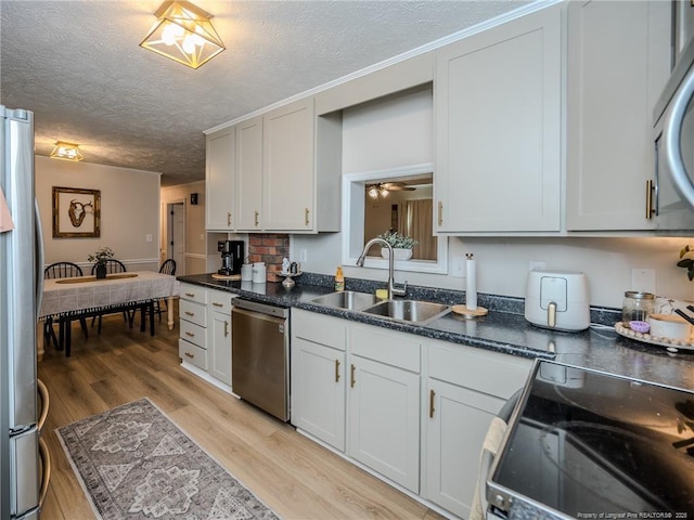 kitchen with light wood-style flooring, a sink, dark countertops, stainless steel appliances, and a textured ceiling