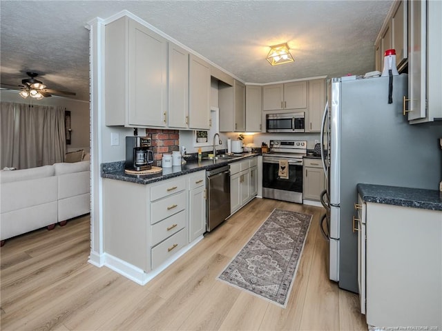 kitchen featuring a sink, stainless steel appliances, a textured ceiling, light wood-style flooring, and a ceiling fan