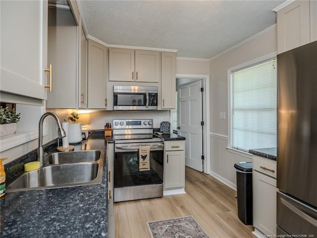 kitchen with a sink, light wood-type flooring, a textured ceiling, appliances with stainless steel finishes, and ornamental molding