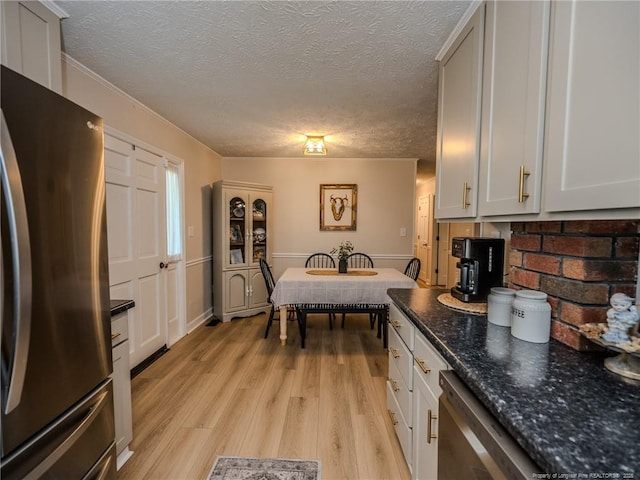 kitchen featuring stainless steel appliances, a textured ceiling, light wood-style flooring, and dark stone countertops