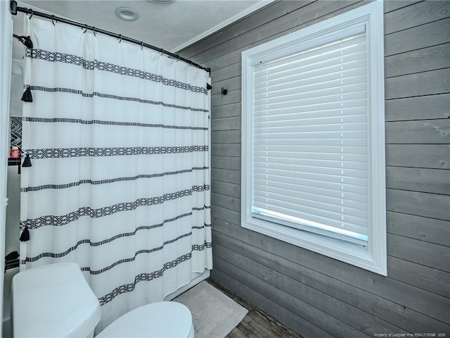 full bathroom featuring curtained shower, wooden walls, toilet, and wood finished floors