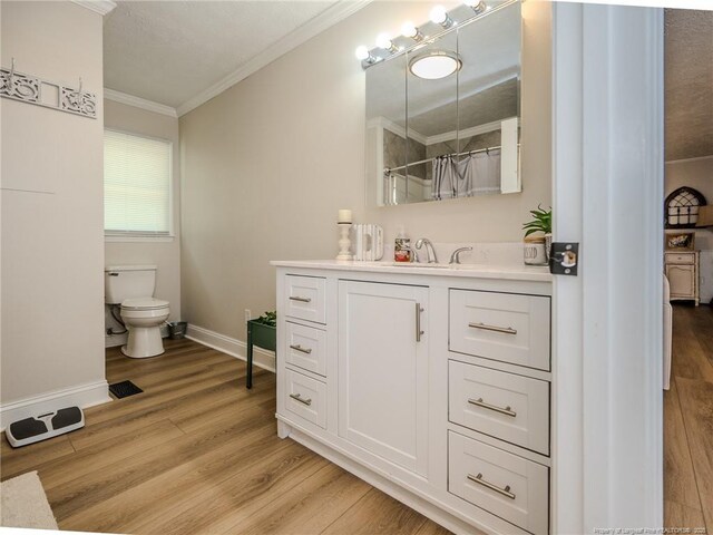 bathroom featuring toilet, wood finished floors, vanity, crown molding, and baseboards