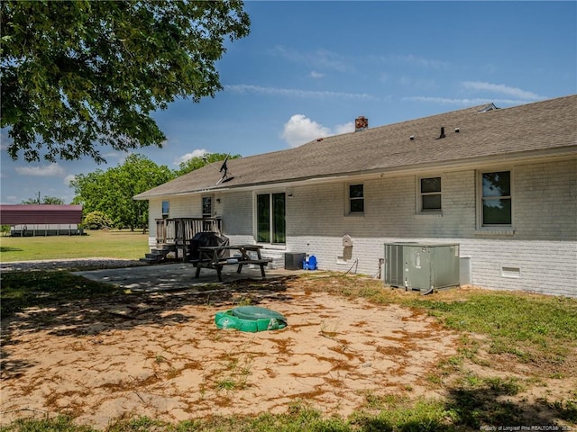 back of house with a chimney, a lawn, brick siding, a patio, and central AC unit