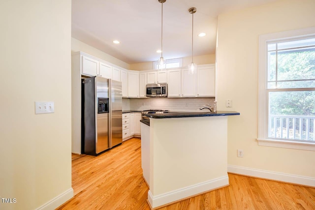 kitchen featuring appliances with stainless steel finishes, dark countertops, light wood-style flooring, white cabinets, and a peninsula