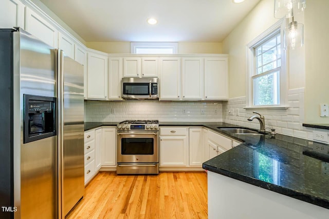 kitchen featuring appliances with stainless steel finishes, a sink, white cabinets, light wood finished floors, and tasteful backsplash