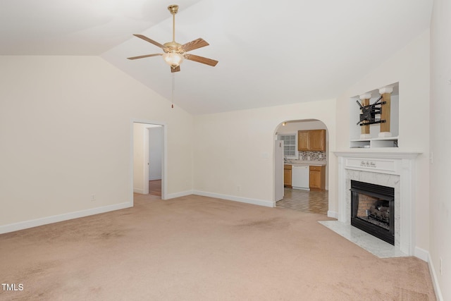 unfurnished living room with vaulted ceiling, light colored carpet, a ceiling fan, arched walkways, and a premium fireplace