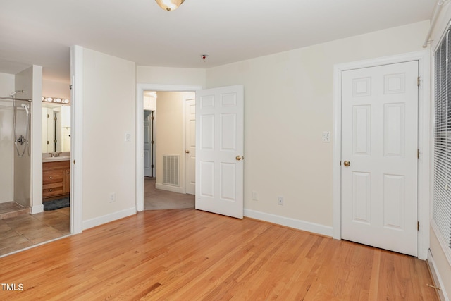 unfurnished bedroom with light wood-style flooring, a sink, baseboards, and ensuite bathroom