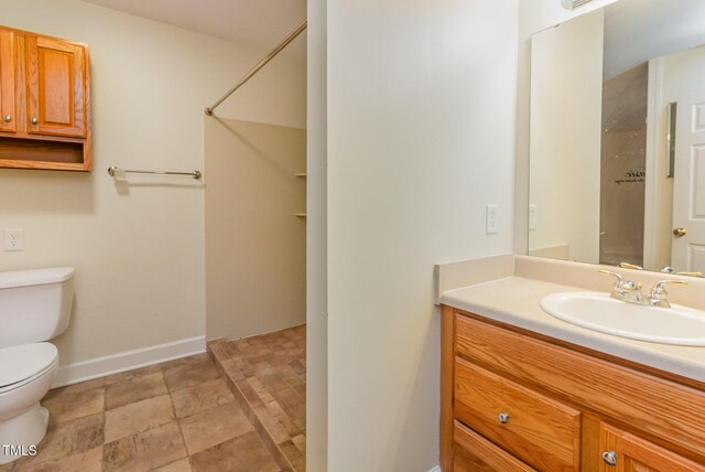 full bath with toilet, stone finish flooring, baseboards, vanity, and a shower