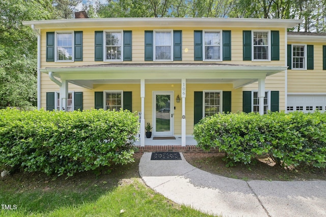 colonial house featuring a chimney, covered porch, and a garage