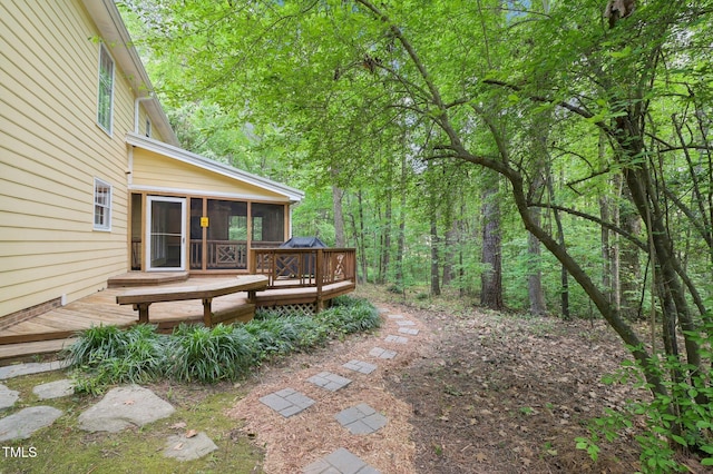 view of yard with a sunroom, a forest view, and a wooden deck