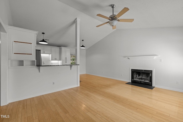 unfurnished living room featuring ceiling fan, a fireplace with flush hearth, light wood-style flooring, vaulted ceiling, and baseboards