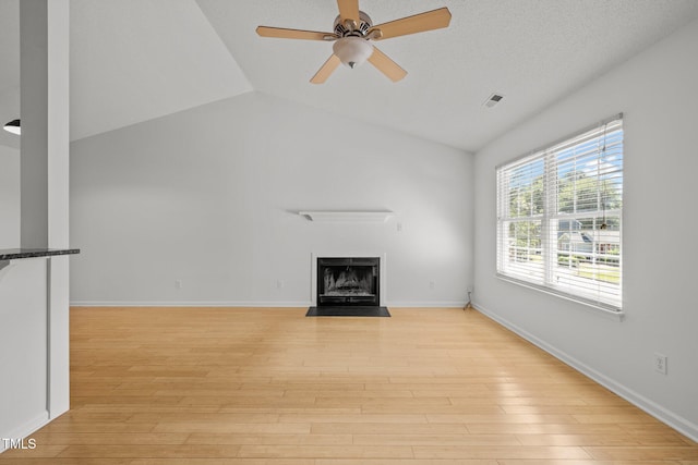 unfurnished living room featuring lofted ceiling, a fireplace with flush hearth, light wood-style flooring, ceiling fan, and baseboards