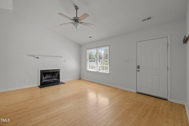 unfurnished living room featuring ceiling fan, vaulted ceiling, a fireplace with flush hearth, light wood-type flooring, and baseboards