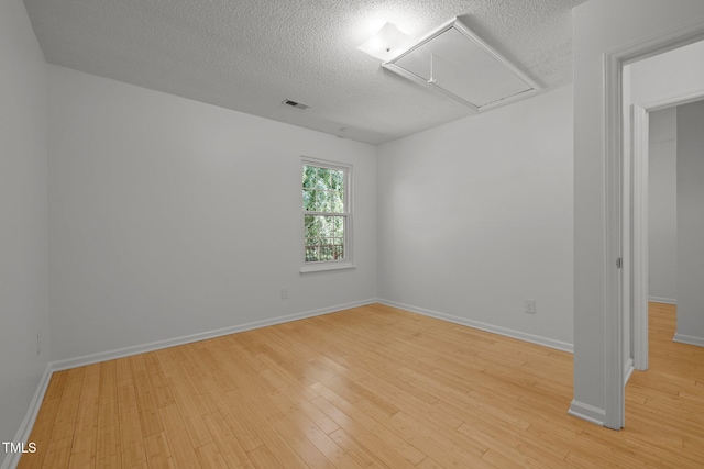 spare room featuring attic access, a textured ceiling, light wood finished floors, and baseboards