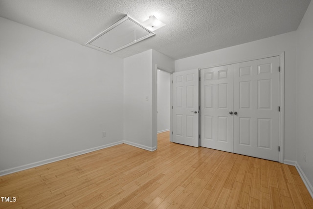 unfurnished bedroom featuring attic access, a textured ceiling, light wood-style floors, a closet, and baseboards