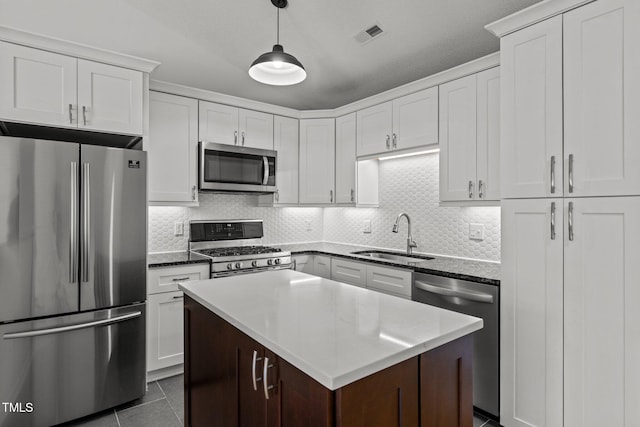kitchen featuring appliances with stainless steel finishes, a sink, tasteful backsplash, white cabinets, and a center island