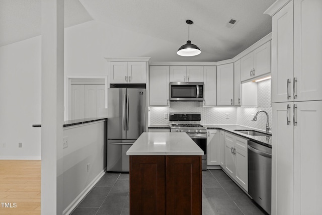 kitchen featuring appliances with stainless steel finishes, a sink, tasteful backsplash, white cabinetry, and vaulted ceiling
