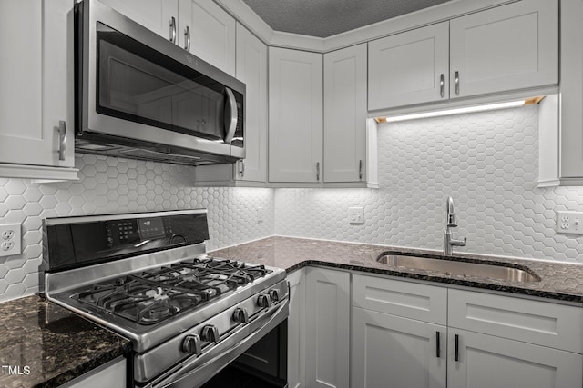 kitchen with stainless steel appliances, a sink, tasteful backsplash, and dark stone counters