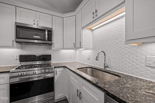 kitchen featuring appliances with stainless steel finishes, a sink, backsplash, dark stone counters, and a textured ceiling