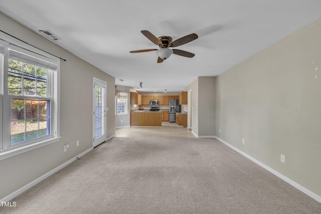 unfurnished living room featuring a ceiling fan, baseboards, and light carpet