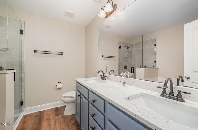 bathroom with baseboards, a stall shower, wood finished floors, toilet, and double vanity