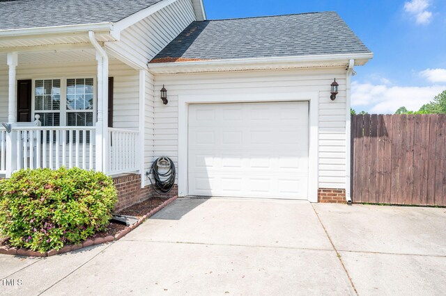 property entrance with roof with shingles, covered porch, driveway, fence, and an attached garage