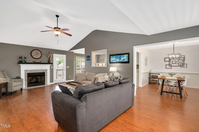 living area with vaulted ceiling, wood finished floors, ceiling fan, a chandelier, and a fireplace