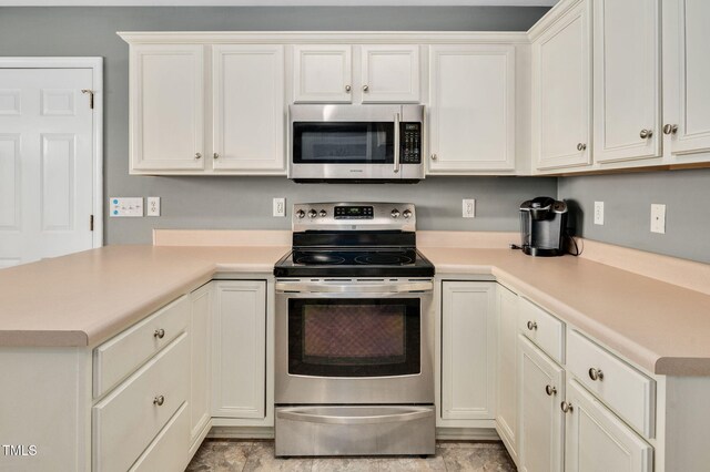 kitchen with appliances with stainless steel finishes, light countertops, a peninsula, and white cabinets